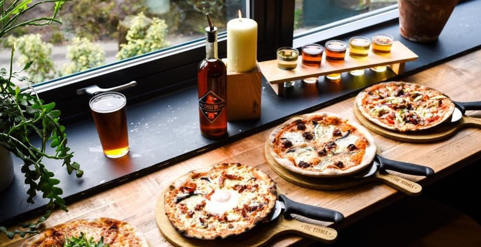 Three pizzas on paddles with beer and serving oils